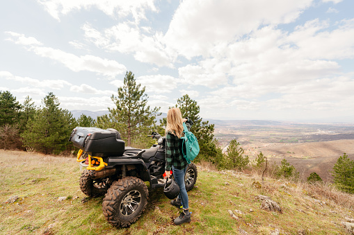 Photo of a young adventurous woman reaching the hilltop with her quad bike, and looking for a new adventure