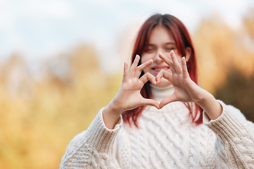 Laughing girl shows hands in the shape of a heart. Joy, friendliness, love, autumn colors.