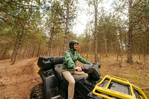 Photo of an adventurous man riding a quad bike down the forest dirt road