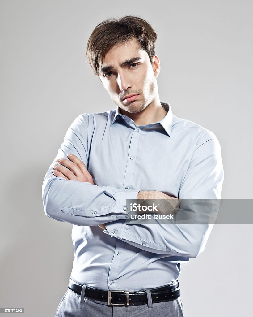Displeasure Portrait of dissatisfied businessman standing against grey background with crossed arms and looking at the camera. Studio shot. 25-29 Years Stock Photo