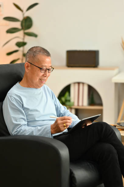 istock Smiling senior man in glasses using digital tablet while sitting on armchair at home 1751742859