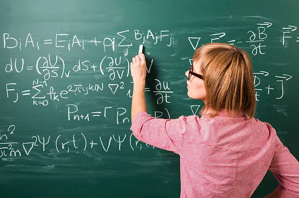 "Close-up on woman in glasses standing against green chalkboard. She explains, solves physics tasks."