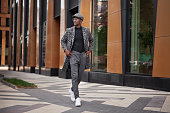 Fashion Man Wearing Fashionable Clothes gray coat animal print, turtleneck, cap, trousers and white sneakers. Outdoors. Male stylish Model walking city Street. Trendy, street fashion outfit