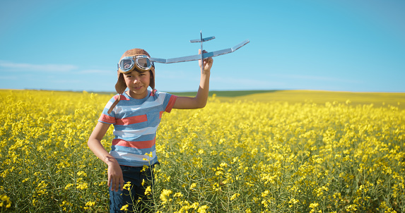 Field, airplane toys and young happy child, boy or fighter pilot fun, weekend youth game or imagine flight, air travel or journey. Blue sky, walking and kid fly plane in daffodil flowers development