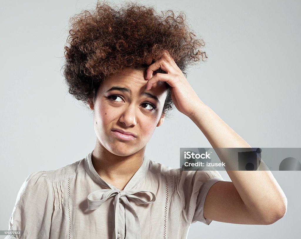 Worried Teen Girl Portrait of teen afro girl looking up with hand in hair. Studio shot, grey background. One Woman Only Stock Photo