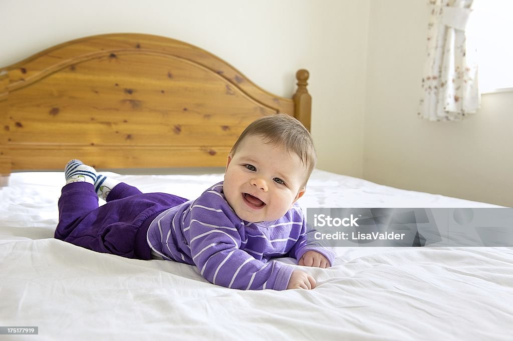 Baby on bed "Young baby aged 4 to 9 months lying on front on double bed, laughing, copy space" Babies Only Stock Photo