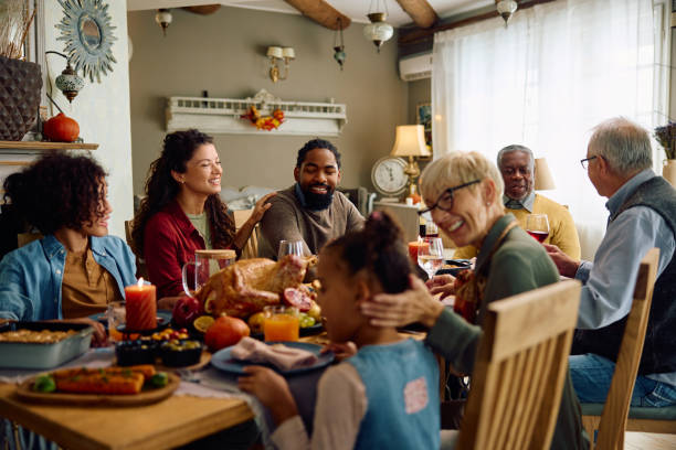Happy multiracial extended family celebrating Thanksgiving at dining table. Happy multigeneration family gathering for Thanksgiving meal at dining table. social interaction stock pictures, royalty-free photos & images