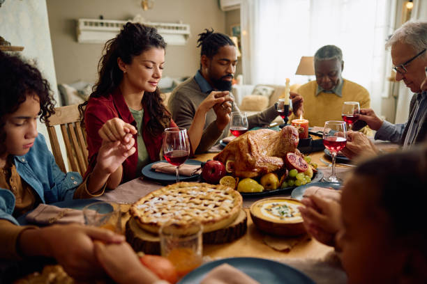 istock Extended family saying grace while gathering for meal at dining table on Thanksgiving. 1751783662