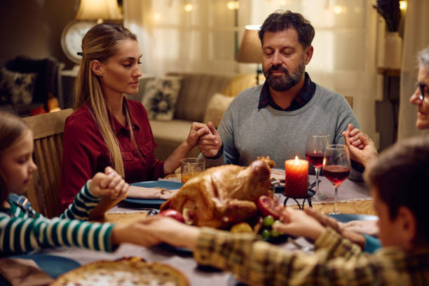 familia extendida orando mientras se toman de la mano en la mesa del comedor en el día de acción de gracias. - family thanksgiving dinner praying fotografías e imágenes de stock