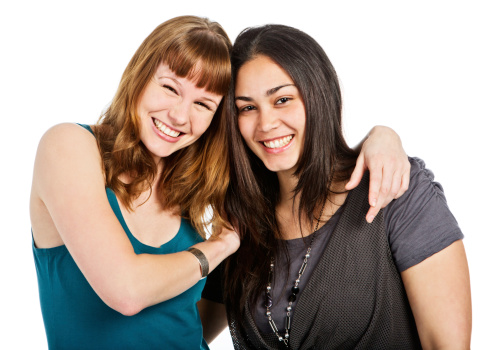 Two beautiful young women laughing happily with their arms round each other in an affectionate embrace. Isolated on white.