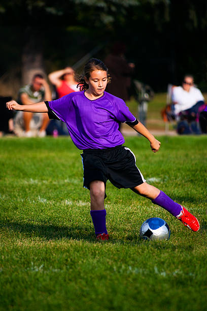 młoda kobieta piłki nożnej gracza z piłką osiągnie stopy - soccer action child purple zdjęcia i obrazy z banku zdjęć
