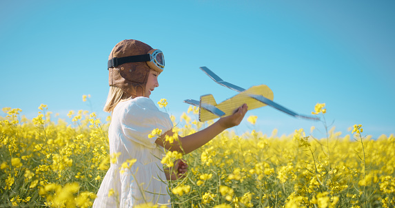 Outdoor field, plane toys and happy kid, girl or youth smile for gift present, fun fantasy games and play pretend in nature. Flight trip pilot, natural daisy flowers and child fly airplane in spring