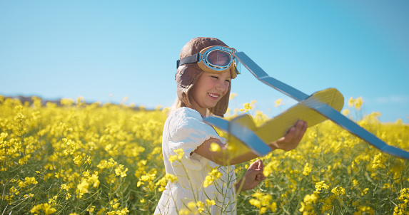 Field, plane toys and child happy, outdoor and smile for childhood, fun fantasy games or play pretend flight in nature. Travel pilot, flowers and youth kid adventure, freedom and fly airplane model