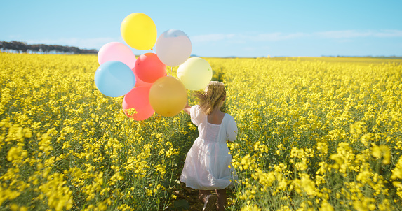 Walking, field and a person with balloons in spring for a party, birthday or freedom. Summer, back and a girl with decoration for celebration, summer or color in nature, countryside or a park