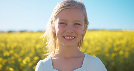 Smile, portrait and child in field of flowers with blue sky, countryside and natural spring wellness. Nature, happiness and face of girl in floral grass with peace, freedom and adventure with plants
