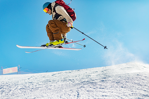 Young adult man skiing in mountain at sunny day, jumping and having fun
