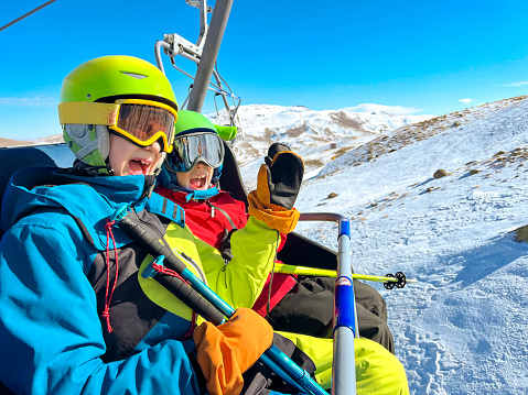 Two brothers skiing in mountain, going up on ski lift and having fun