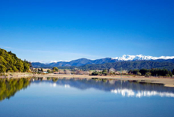 View across the Motueka Estuary, Tasman Region, New Zealand A view across the Motueka Estuary at high tide to a rural scene and the distant snow-covered Kahurangi Ranges in the Tasman Region of New Zealand's South Island. motueka stock pictures, royalty-free photos & images