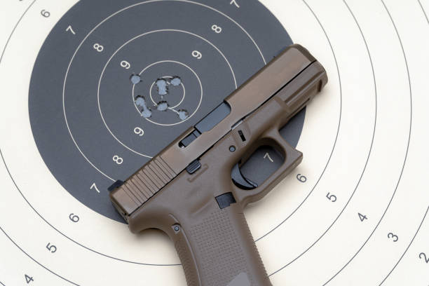 Sand colored pistol on the paper target with a holes from bullets