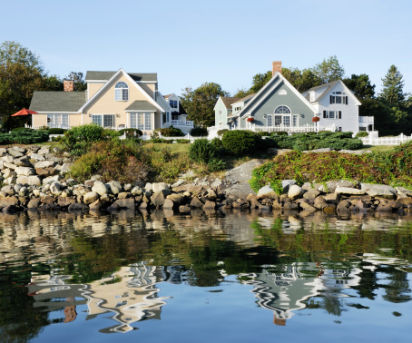 Homes on New England rocky coastline with reflection in sea water.