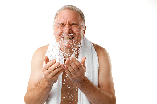 Morning washing. Portrait of attractive middle aged man spraying water on his face against white studio background. Concept of natural beauty, skin and face care, hygiene. Copy space for text, ad