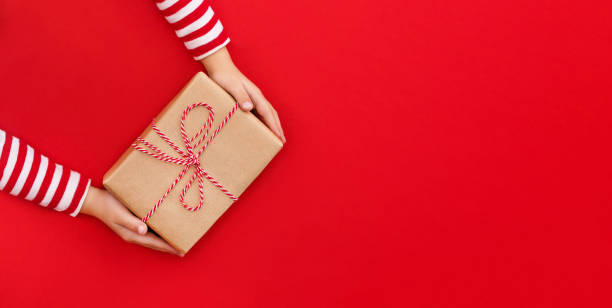 Christmas banner gift box in children's hands on a red background, presenting a gift