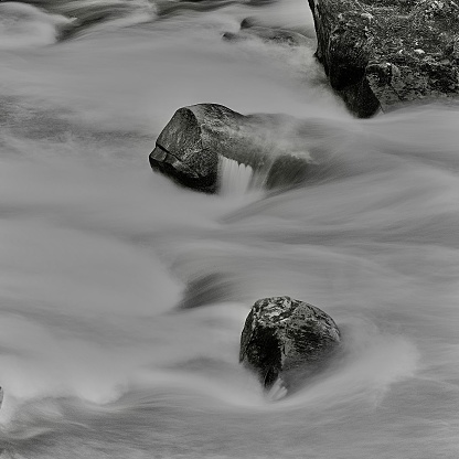 A scenic view of a river with jutting rocks in grayscale
