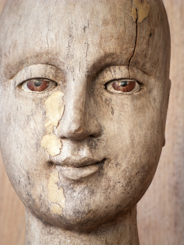 A cropped photograph of a female antique wooden head with glass eyes.
