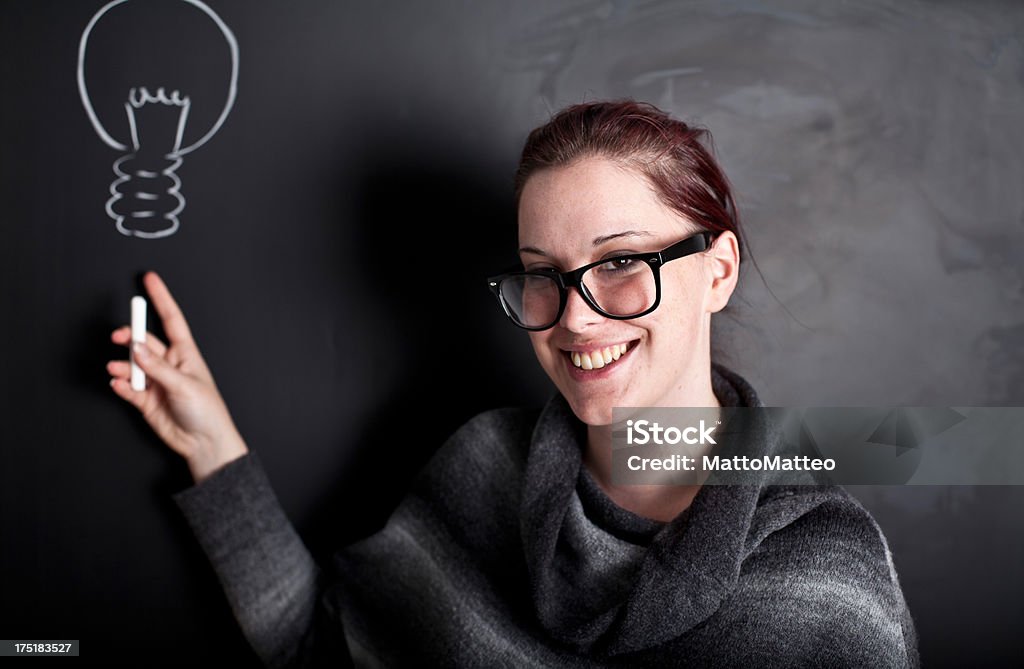 Young woman in front of a chalkboard A young woman wearing glasses stands in front of a chalkboard on which is written something. Adult Stock Photo