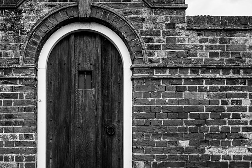 Monochrome view of an old timber door and small window seen on a brick built garden wall and arch. Located at a famous English side town.