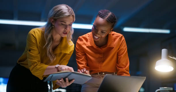 istock Business women, teamwork and notebook for night research, information technology planning or teamwork in office. Professional people, programmer or manager with notes, ideas and proposal for software 1751843416