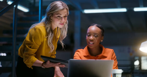 istock Laptop, teamwork and coaching, women in dark office together with tablet, advice and web search. Night, tech business and woman with manager at desk for research, review or help with feedback online. 1751843417