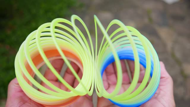 POV: a rainbow coil spring. A person playing with a slinky. Person playing with a spiral toy. lastic colorful spring. Plastic coil spring toy