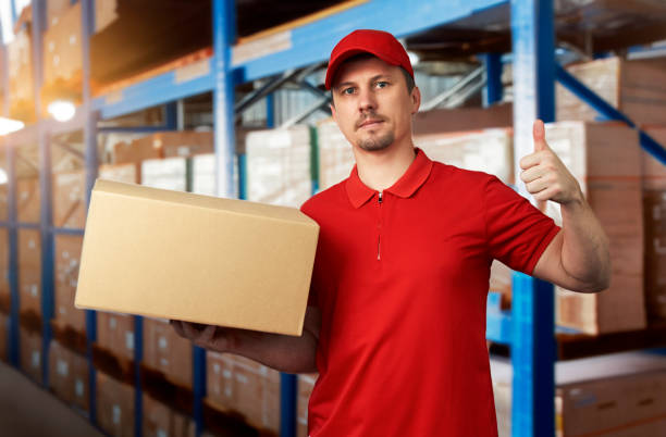 istock Young delivery man in red uniform standing with parcel box 1751857423