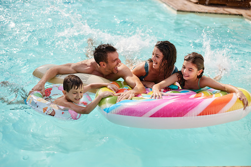 Carefree parents and their kids having fun during summer day in the swimming pool.