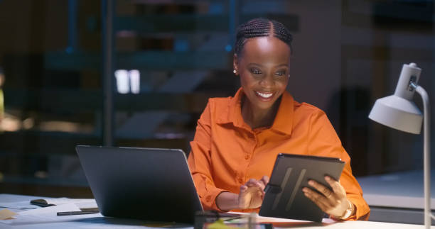istock Business woman, tablet and computer for night data analytics, happy results and multimedia comparison in office. African worker on digital technology, laptop and software, statistics or online report 1751859748