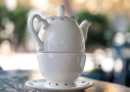 A white porcelain teapot superimposed on the classically shaped mug against a blurred background