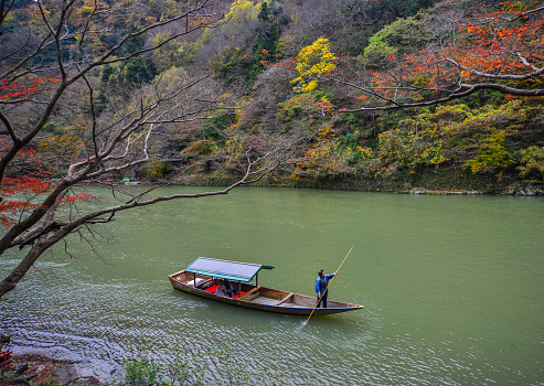 Kyoto, Japan - Nov 28, 2016. A man rowing boat on river at Arashiyama in Kyoto, Japan. Arashiyama is a nationally designated Historic Site and Place of Scenic Beauty.