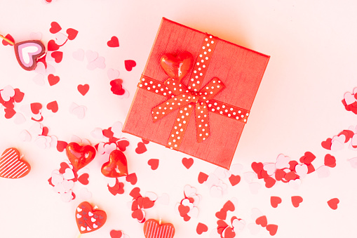 Valentines day festive background with pink hearts and red gift box over pink background close up