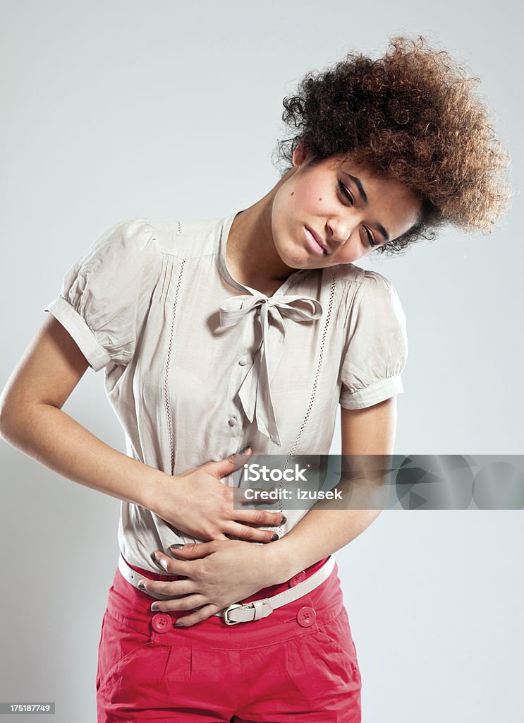 Stomach ache Portrait of teenaged girl suffering from stomach ache. Studio shot, grey background. One Woman Only Stock Photo