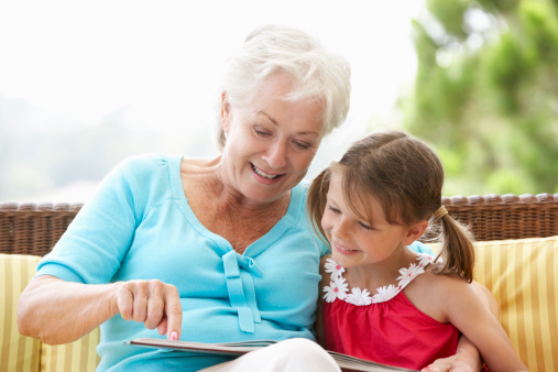 Grandmother And Granddaughter Reading Book On Garden Seat Together