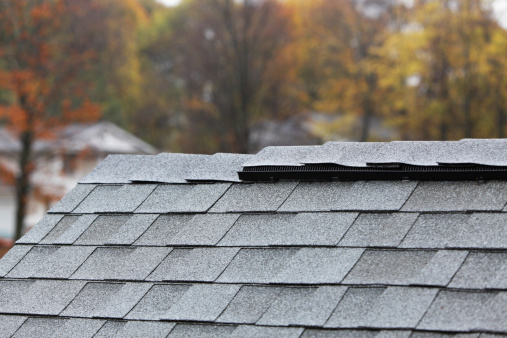 Heavy autumn rain is falling on a newly installed residential asphalt shingle roof with a modern ridge vent running along the roofline.