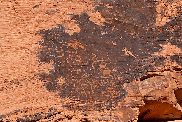 Ancient Petroglyphs on the Canyon Wall Valley of Fire is Nevada’s oldest state park. The park gets its name from the red rock formations which appear to be on fire as the sun sets. These Aztec sandstone rocks were formed from sand dunes 150 million years ago. The region was further shaped by uplifting and faulting followed by extensive erosion. The Anasazi people visited this area from about 300 BC to 1150 AD. Scarcity of water would have prevented their living here but they probably hunted, gathered food and performed religious ceremonies. There are several sites where their petroglyphs can still be seen. In 1931, 8,760 acres of federal land was transferred to the state of Nevada. In 1933, the Civilian Conservation Corps (CCC) began developing the park which opened in 1934. The CCC continued working on the park into the early 1940’s and built campgrounds, trails, visitor cabins, ramadas and roads. In 1935, the Nevada State Legislature designated the area as Valley of Fire State Park. In 1968, the park was recognized as a National Natural Landmark. This scene of ancient petroglyphs was photographed at Petroglyph Canyon. Valley of Fire State Park is located 50 miles northeast of Las Vegas near Overton, Nevada, USA. jeff goulden valley of fire state park stock pictures, royalty-free photos & images