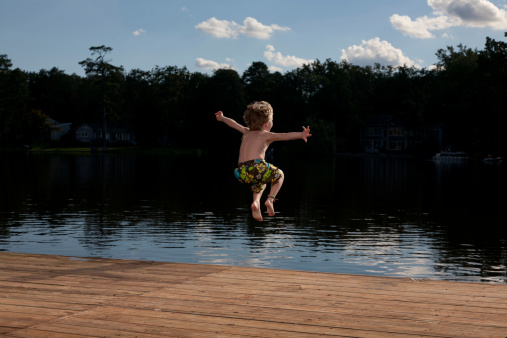 Little boy jumping off a summertime dock and into a public lake