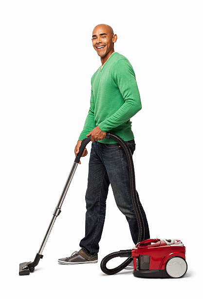 Full length portrait of an African American man cleaning floor with vacuum cleaner. Vertical shot. Isolated on white.
