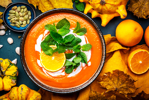 Sweet autumn pumpkin soup with cream, tangerine and mint. Winter healthy vegetarian comfort slow food. Soup bowl on green table background. Top view