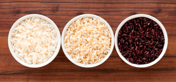 Top view of three bowls containing boiled rice varieties (white, brown and black)