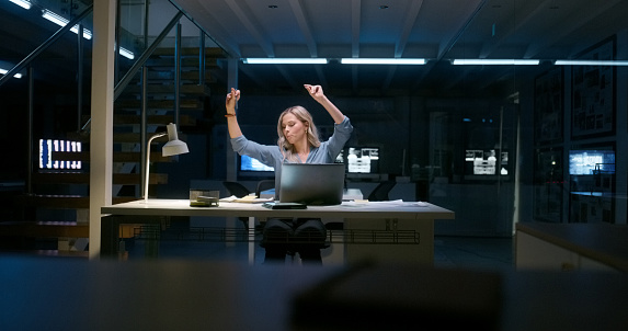 Excited woman, dancing and celebration at night for success, achievement or competition at office. Happy female person working late with smile for winning, victory or bonus promotion at workplace