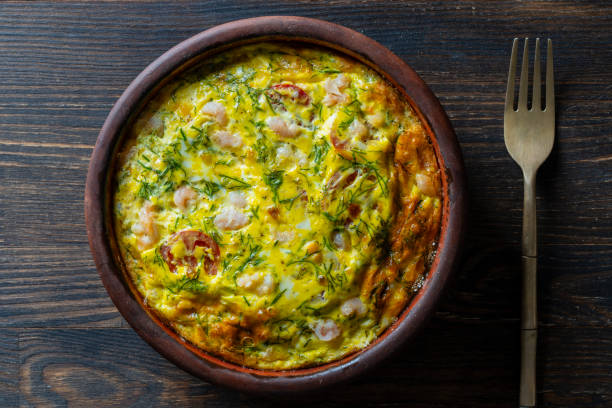 istock Ceramic bowl with vegetable frittata, simple food. Frittata with egg, tomato, pepper, onion, shrimps and cheese on wooden table, closeup, top view. Italian egg omelette 1751931051