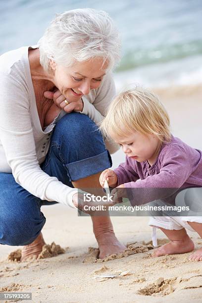 Grandmother And Granddaughter Looking At Shell On Beach Stock Photo - Download Image Now